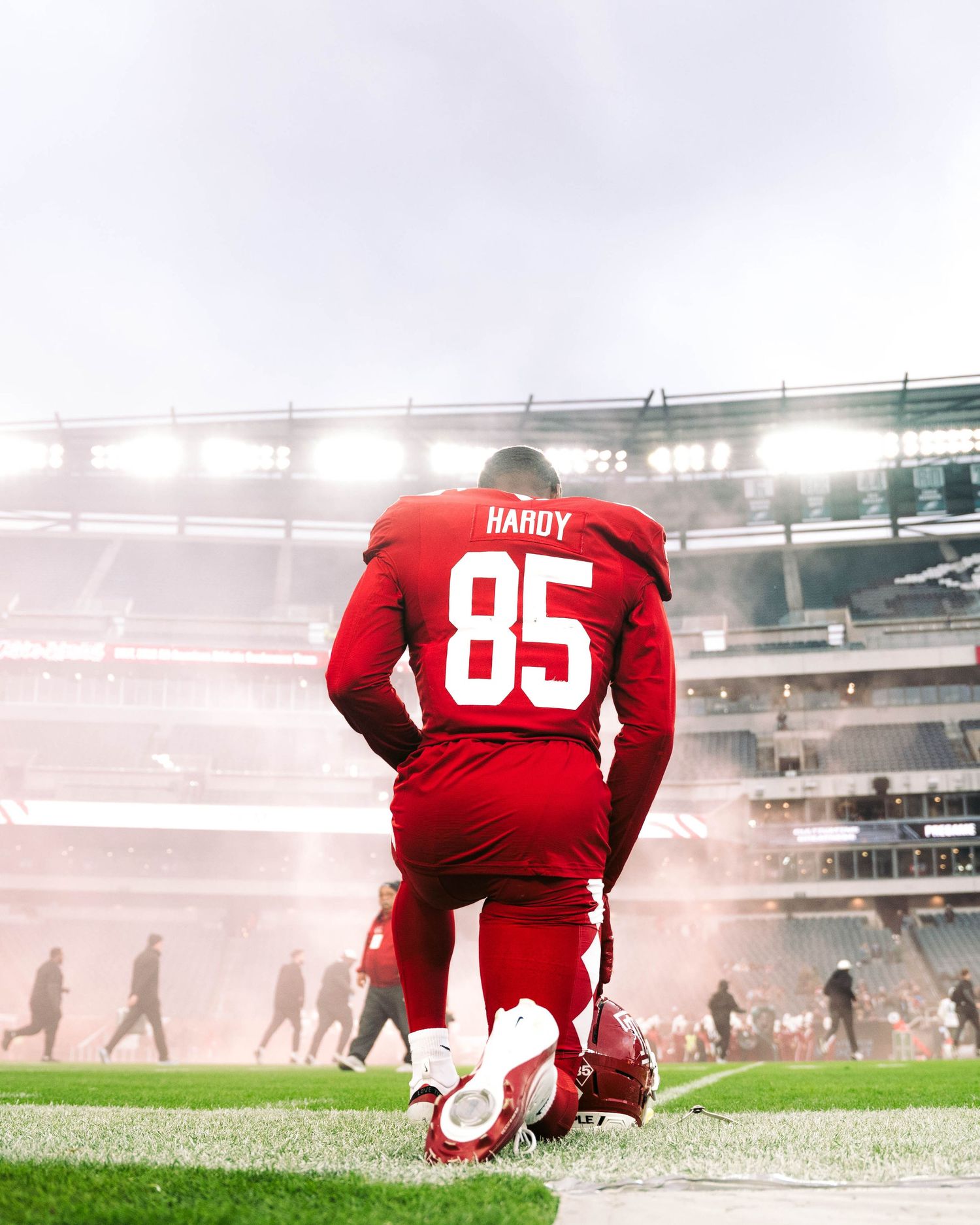 Three soccer players in red jerseys kneel on a misty field during what appears to be a pre-game moment.