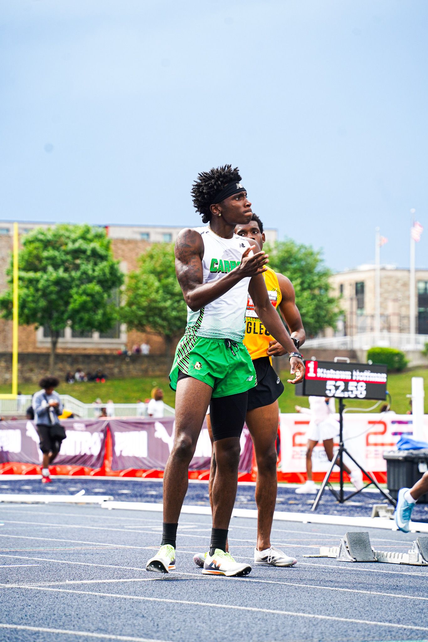 Track athlete in green and yellow uniform crouches in starting position on running track during competition.