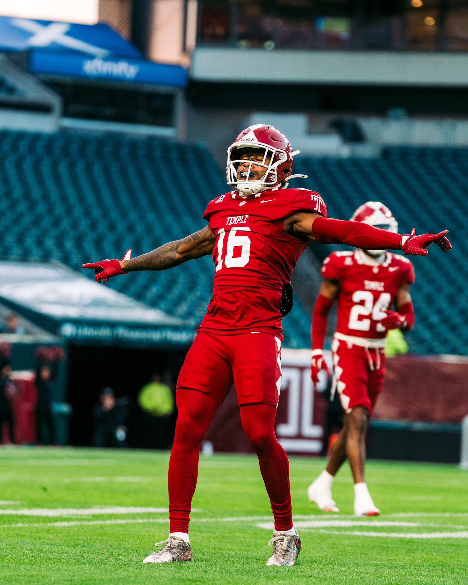 Football players in red uniforms perform stretching exercises on a field during warmup drills.