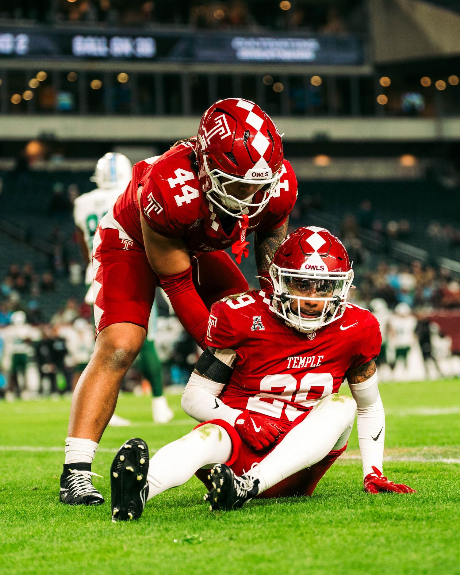Football player in red uniform diving and sliding across green turf field during game action.