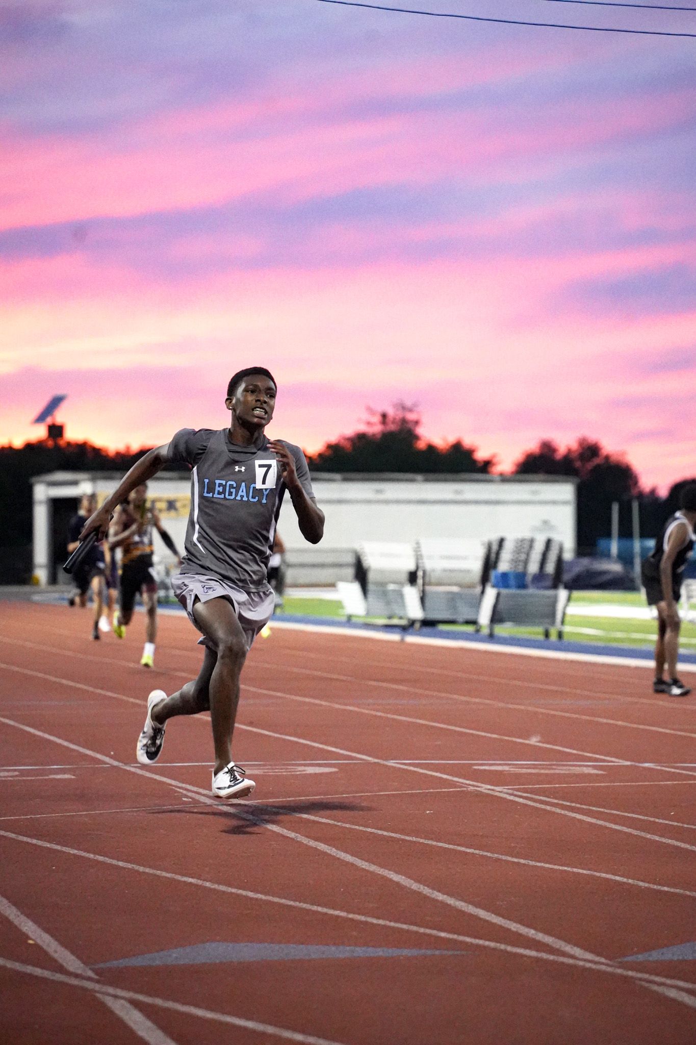 Athletes practice triple jump techniques on an outdoor track during a colorful sunset training session.