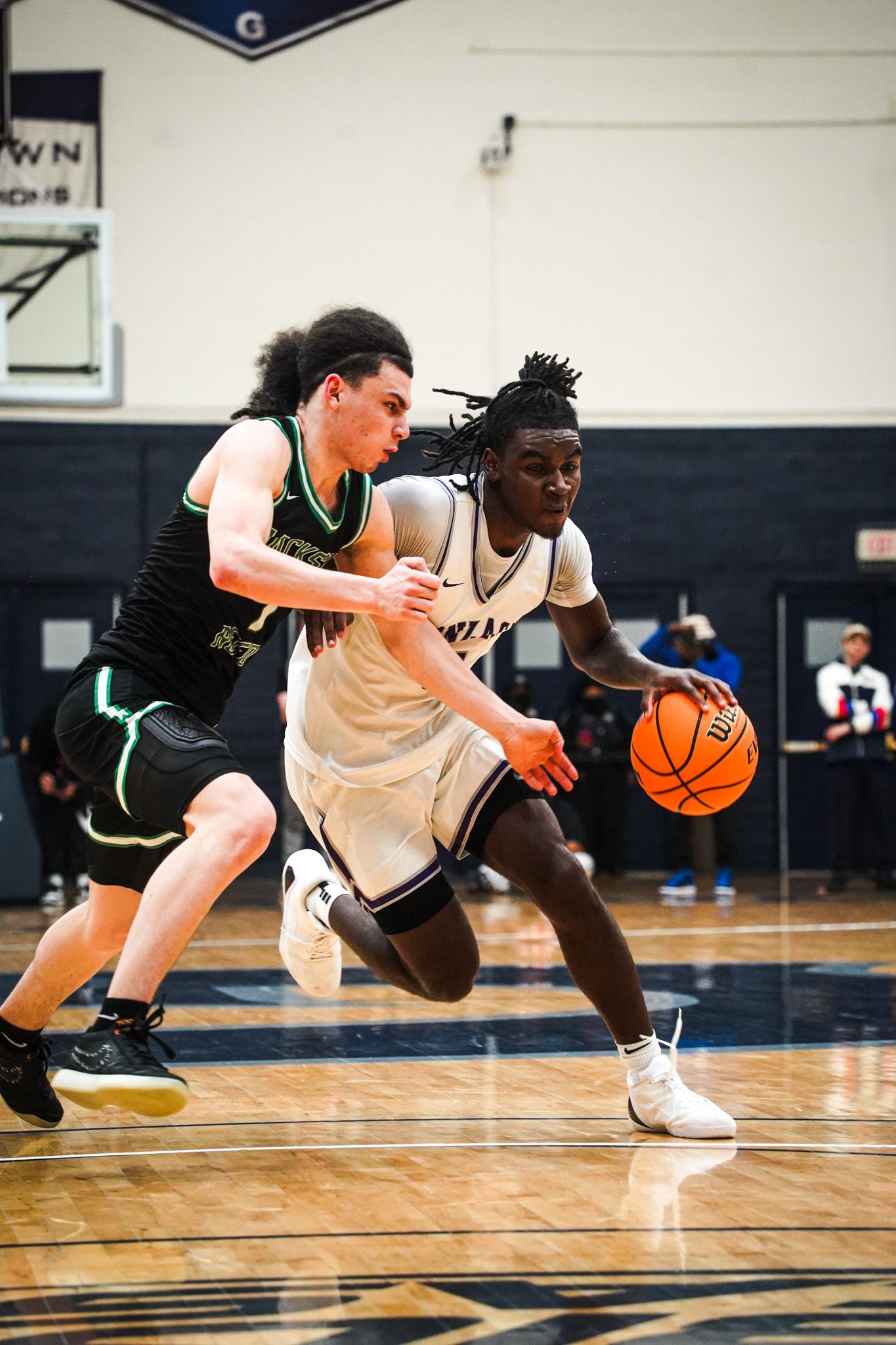 Two basketball players compete intensely for the ball during a competitive game on an indoor court.