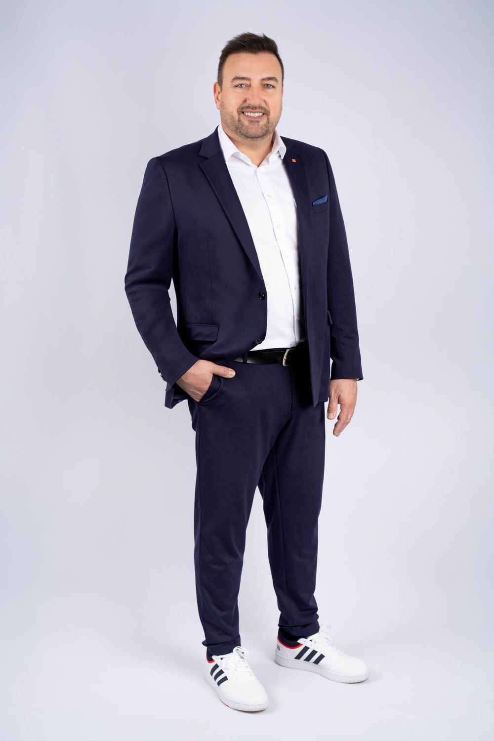 Professional in navy suit and white sneakers poses confidently against light studio background in multiple angles.