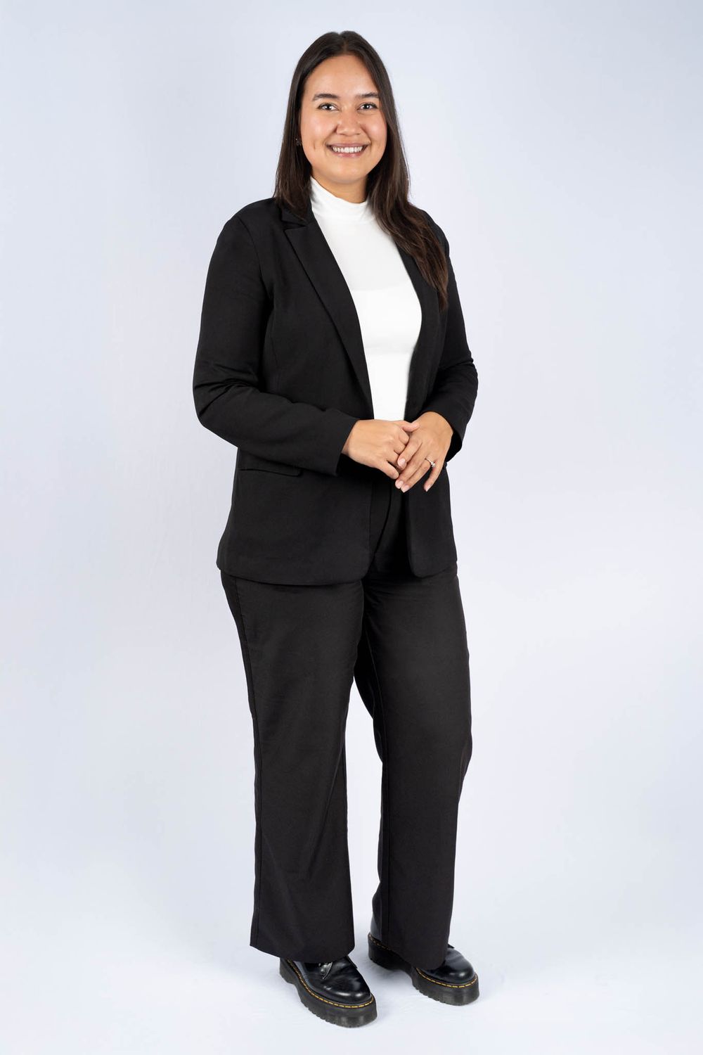 Professional wearing a classic black business suit and white top poses in a studio setting against light background.