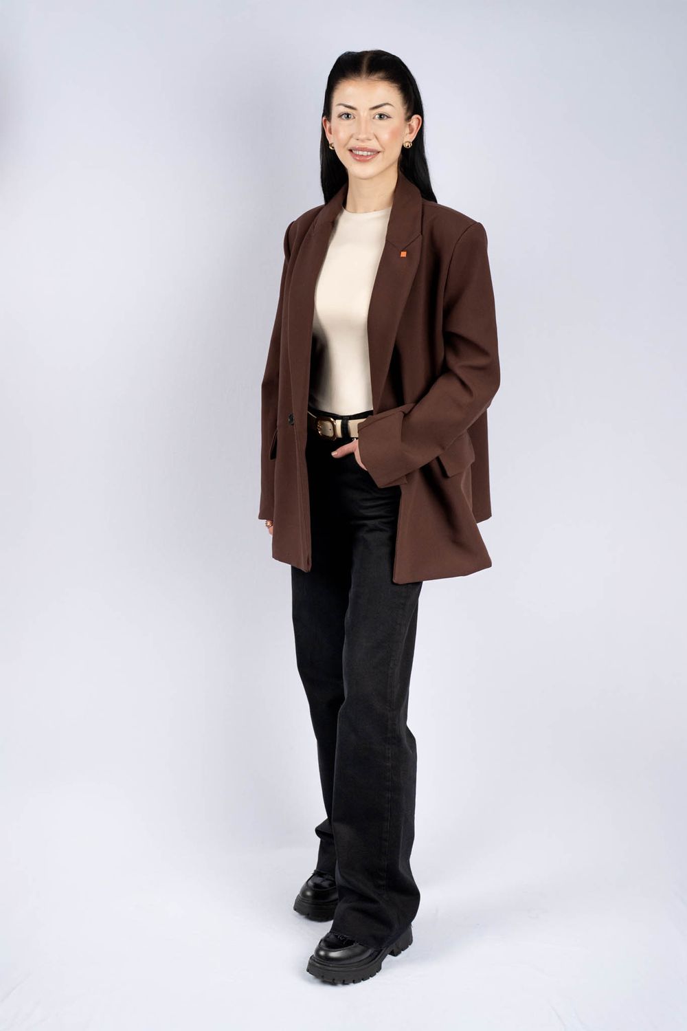 Professional studio shot of a brown blazer and black pants outfit styled with chunky boots against white background.