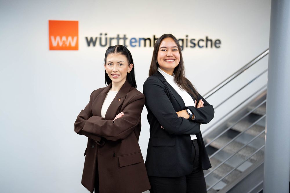 Two business professionals stand smiling on a modern office staircase with Wurttembergische signage visible in background.