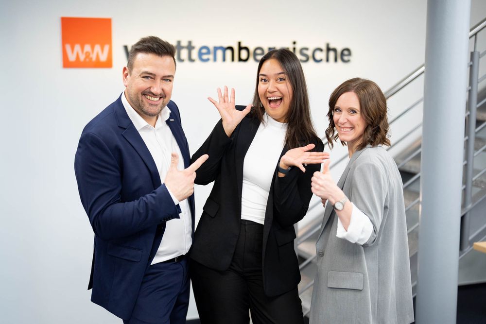Three business professionals in professional attire laughing and gesturing together in an office setting.