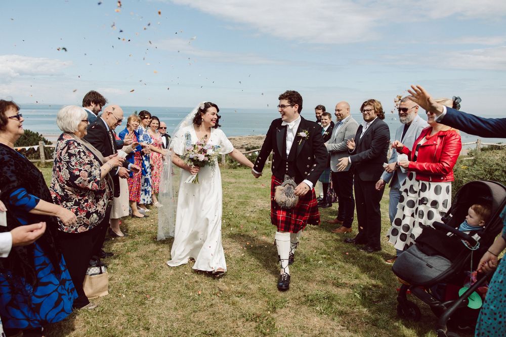 Wedding guests celebrate and dance together in a scenic outdoor meadow setting with mountains in the background.