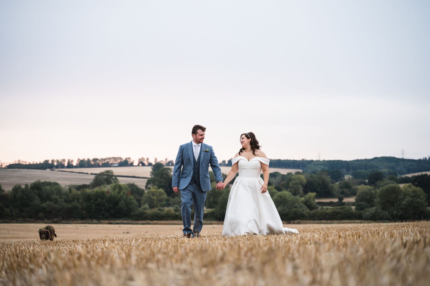 Hollands Farm Weddings Photography with Bride & Groom walking over a field at golden hour