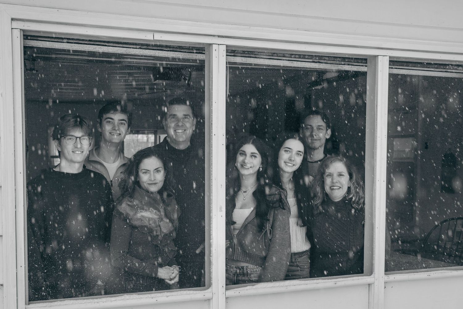 Family gathered together during a winter session in South Haven, smiling through a window with falling snow
