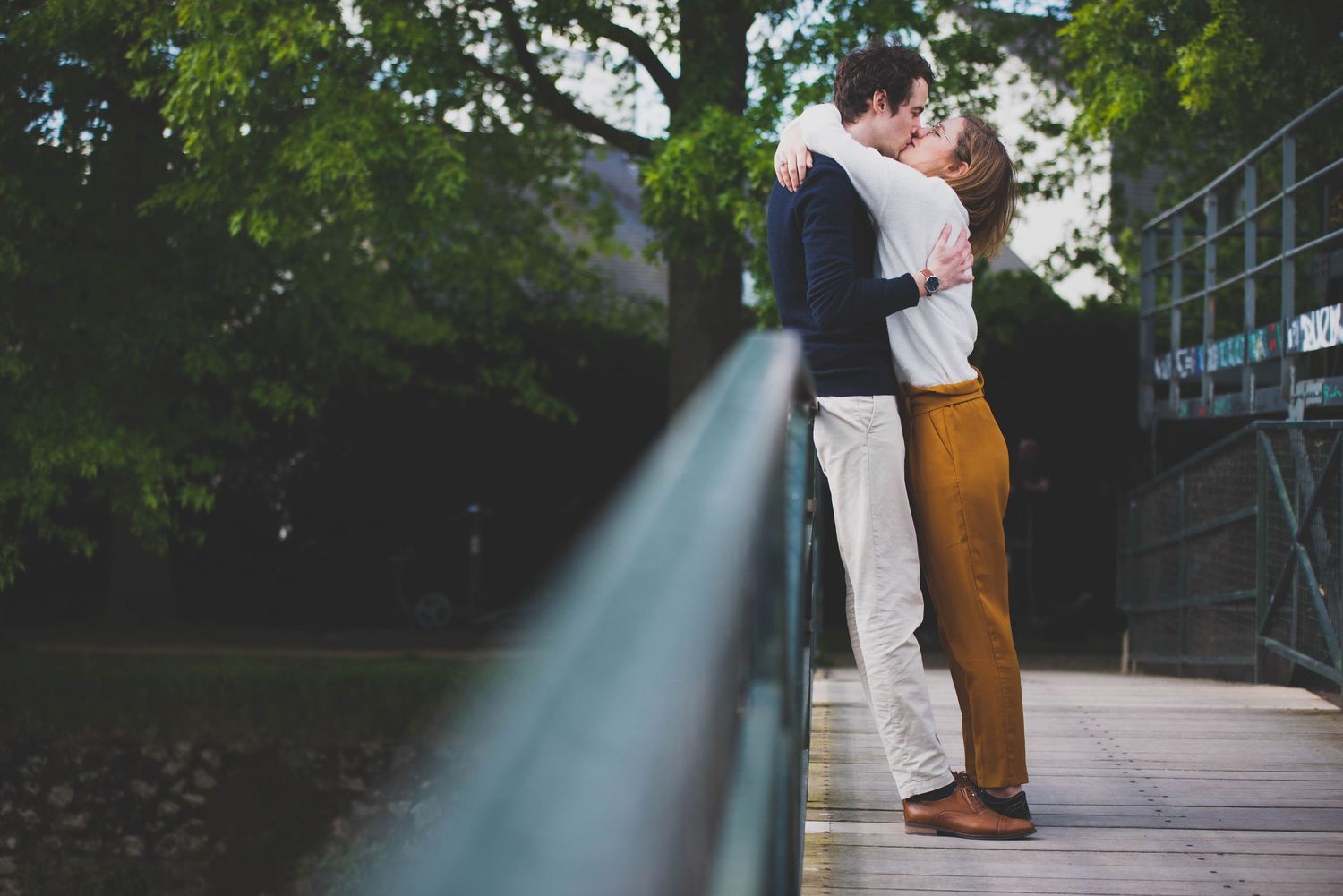 Couple enlacé et s’embrassant sur une passerelle en bois, séance photo engagement en extérieur par photographe en Bretagne.