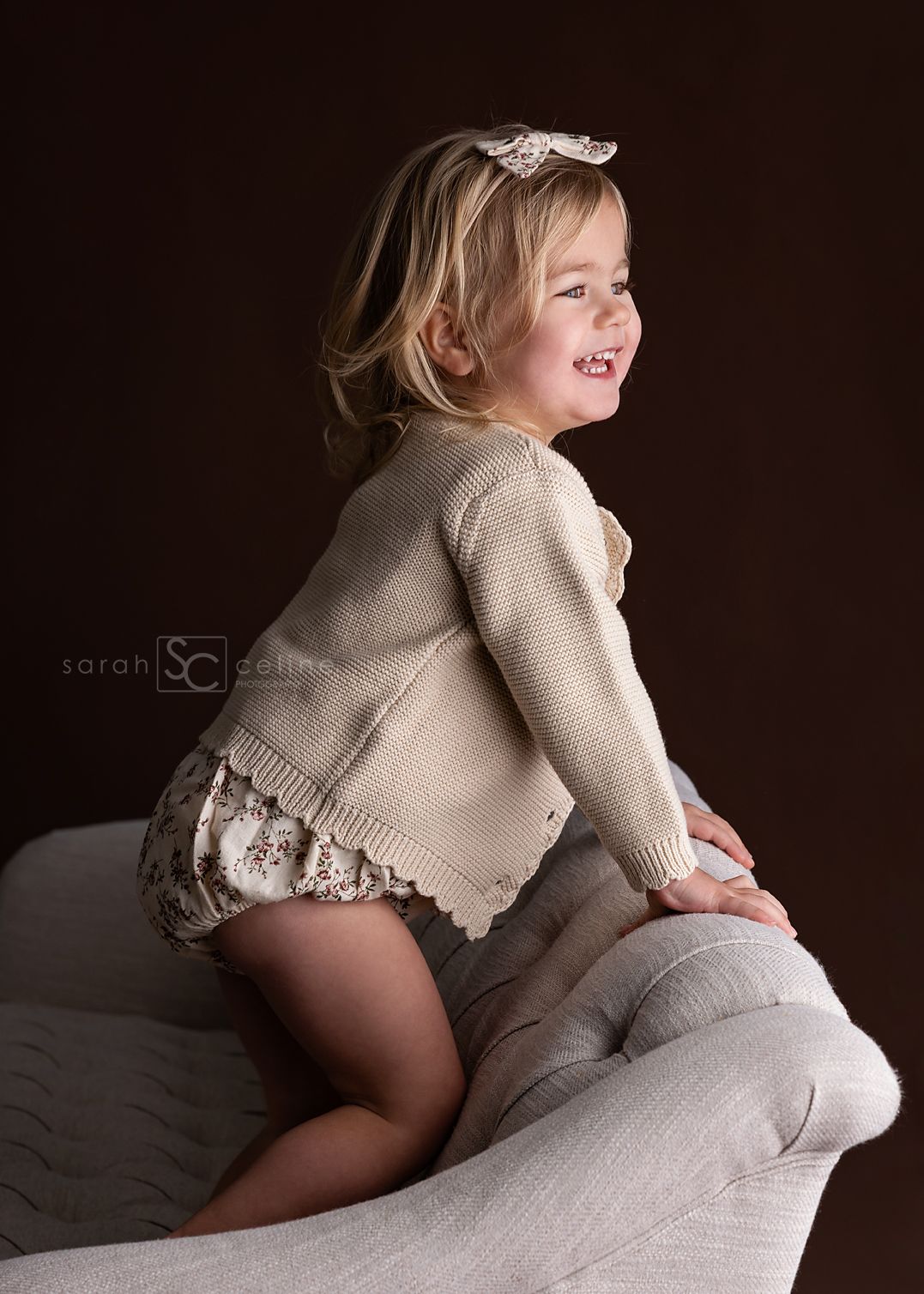 A child in a beige sweater plays and laughs while sitting on white bedding in a series of candid shots.