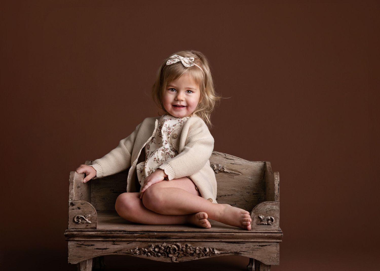 A series of sepia-toned baby portraits showing different poses on a brown cushioned bench.