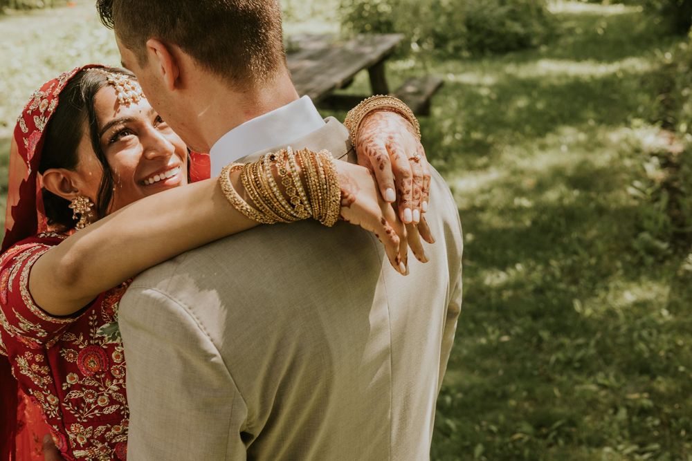A couple in traditional Indian wedding attire share an intimate dance moment in a sunlit outdoor garden setting.