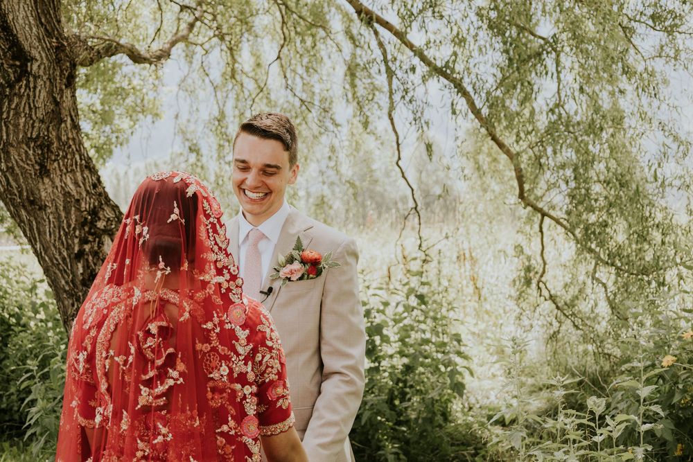 Couple sharing intimate moment under drooping willow tree branches in natural sunlight.