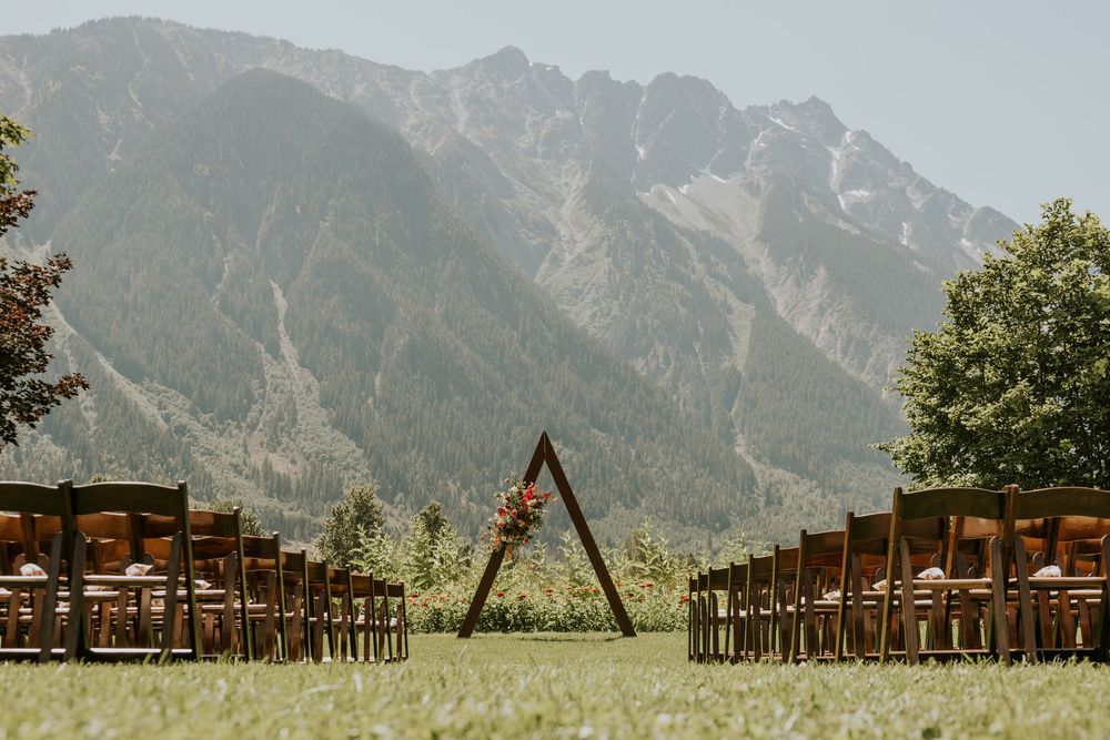 Rustic wooden wedding ceremony setup with mountain backdrop and wooden benches in an outdoor venue.