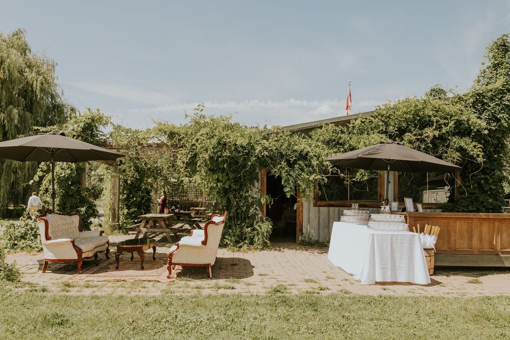 Outdoor wedding venue setup with lounge furniture and umbrellas arranged in a garden setting.