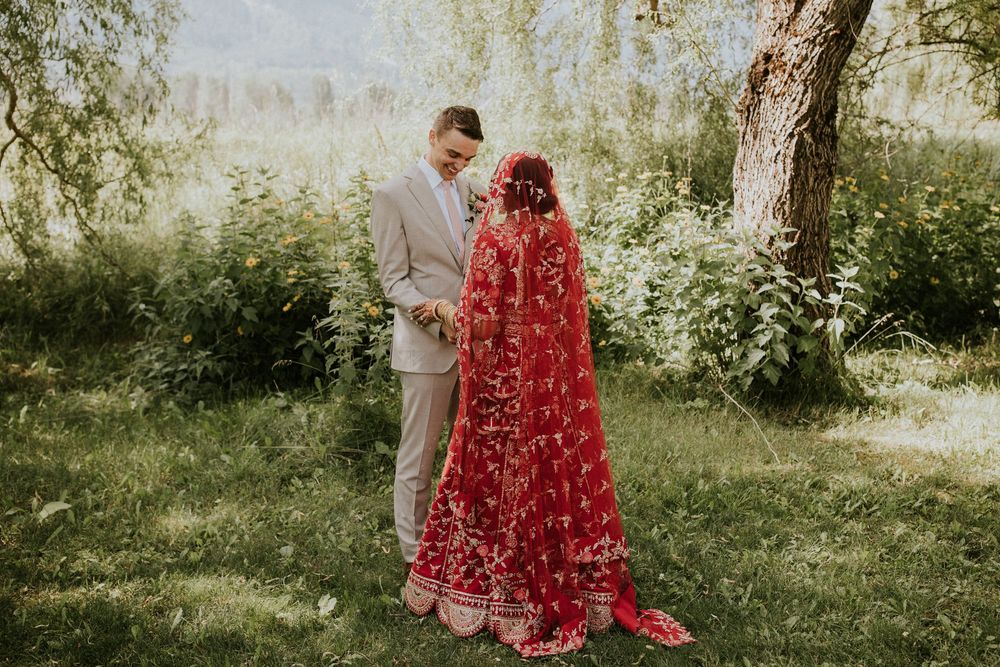 Romantic scene in sunlit meadow with person wearing flowing red dress against mountain landscape.