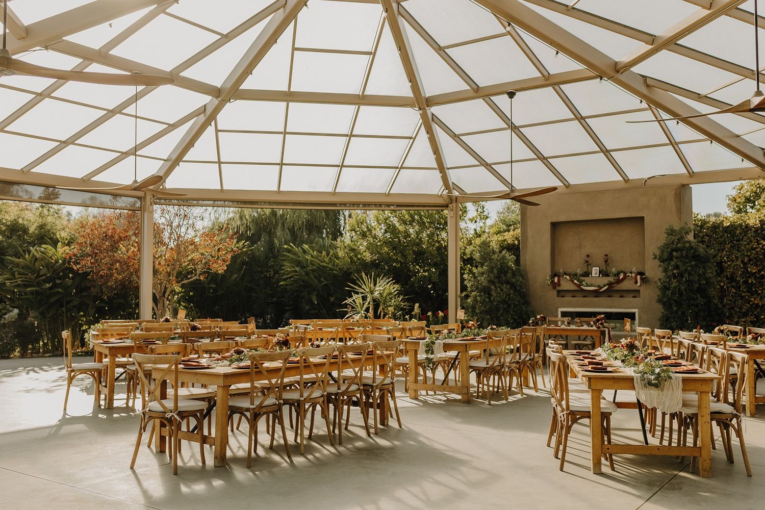 Rustic wooden chairs arranged under an elegant glass-roofed pavilion at River Garden Weddings and Events.