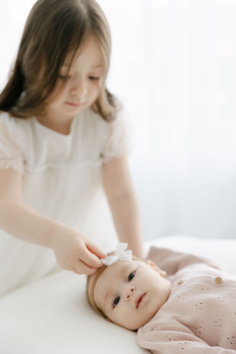 Minimalist newborn photography session showing gentle interactions on white bedding.