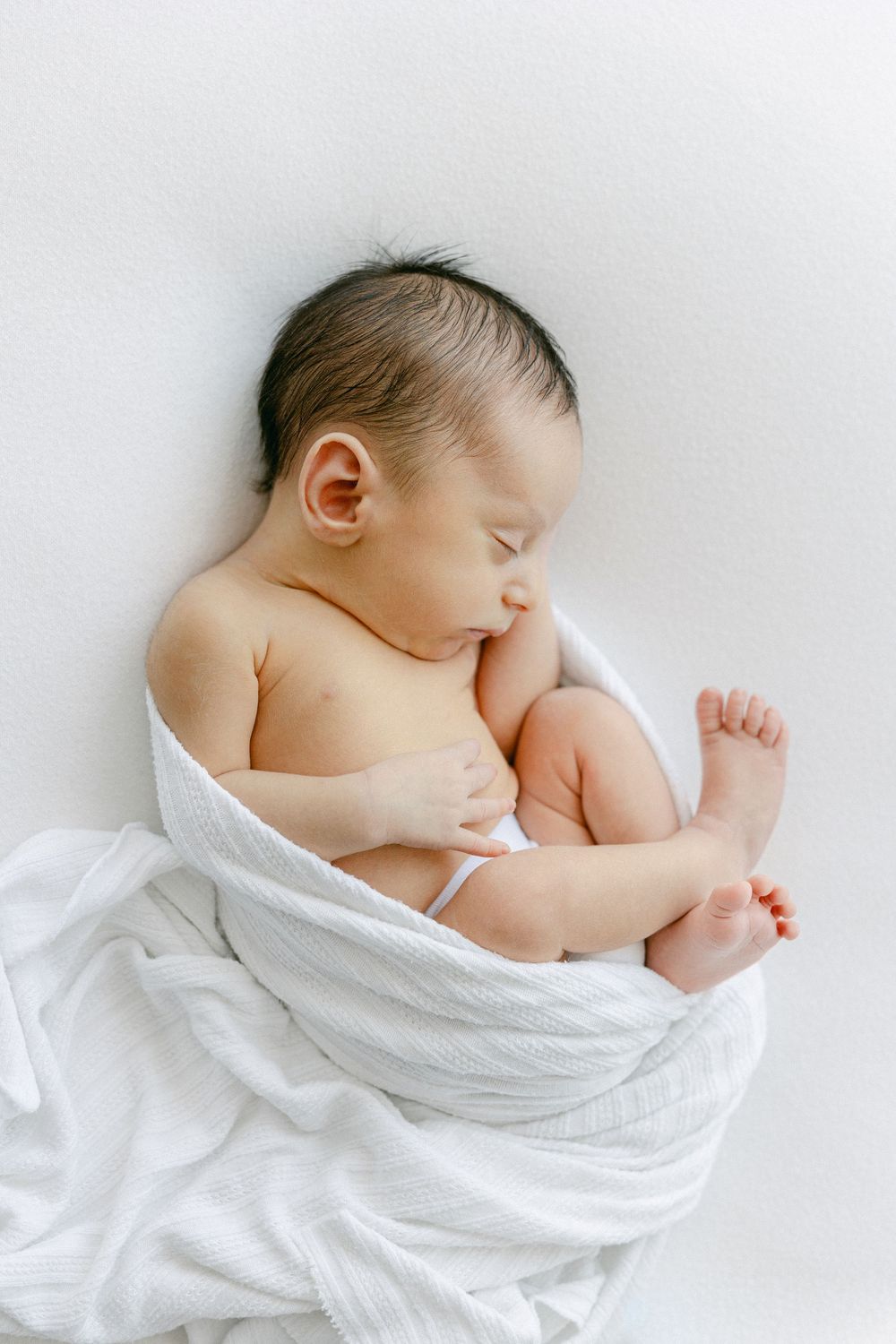 Peaceful sleeping newborn wrapped in white blanket on minimalist background.