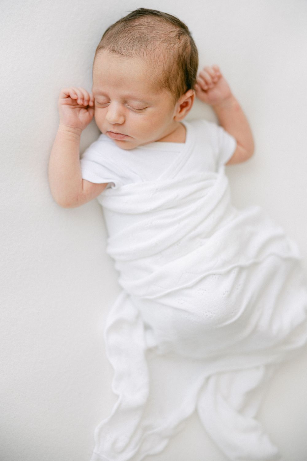 Simple minimalist portraits of sleeping newborn in white against light background.