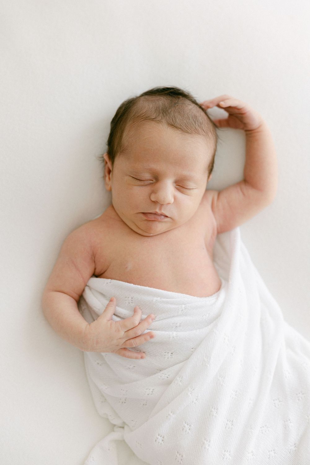 Artistic newborn photography showing peaceful sleeping baby wrapped in white.