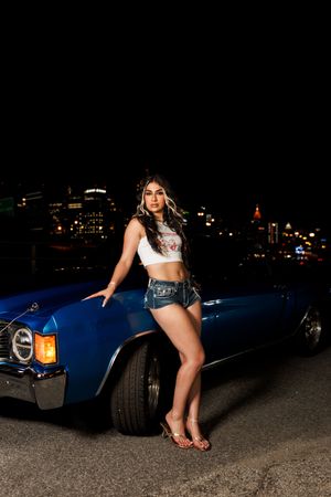 Classic blue convertible car photoshoot at night with city lights in background.