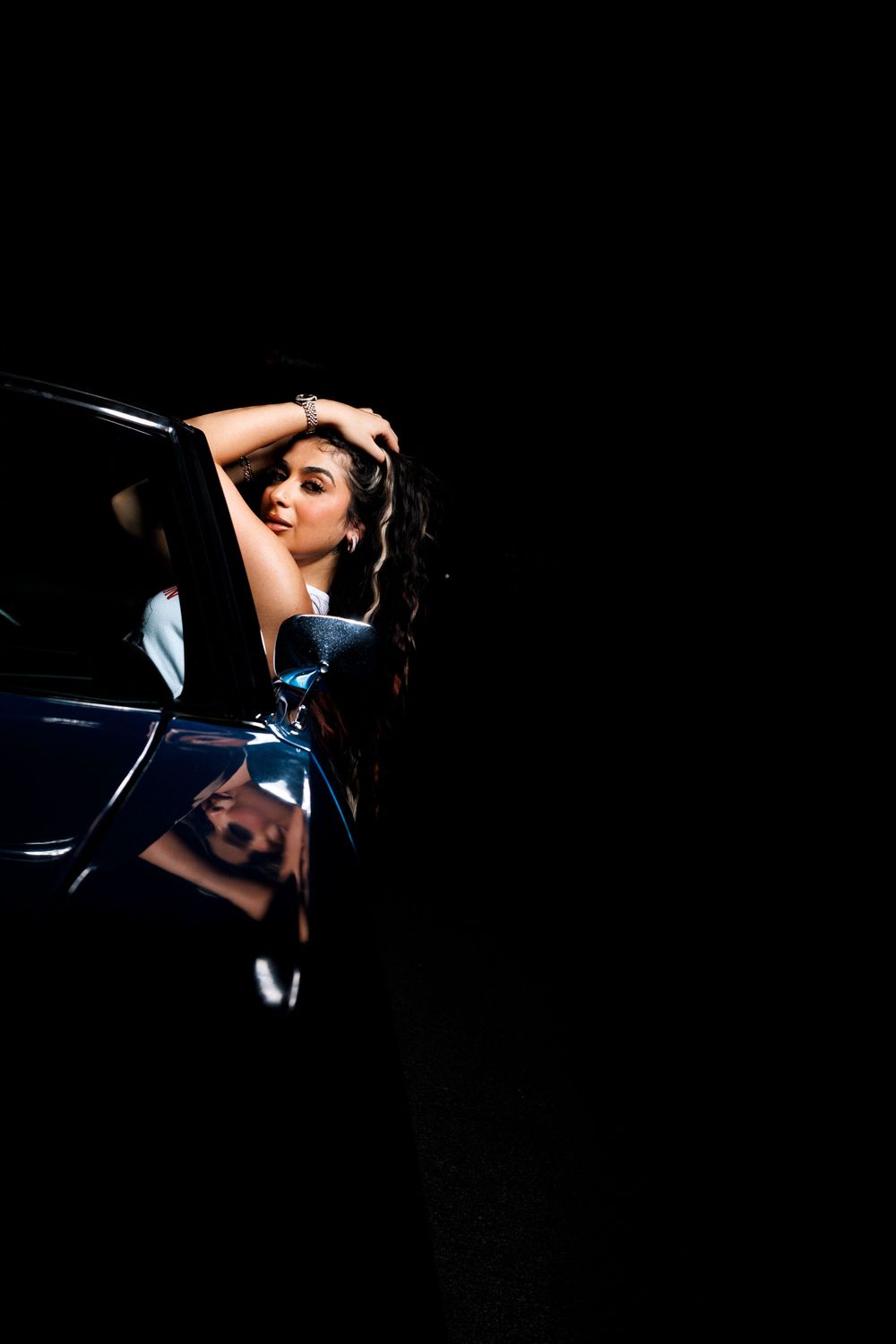 Artistic night portrait with dramatic shadows against blue car exterior.