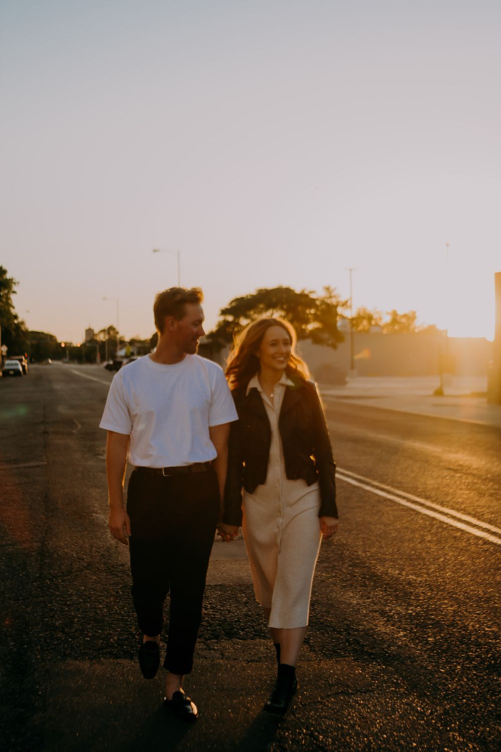 Happy couple holding hands walking on road during golden sunset hour together.