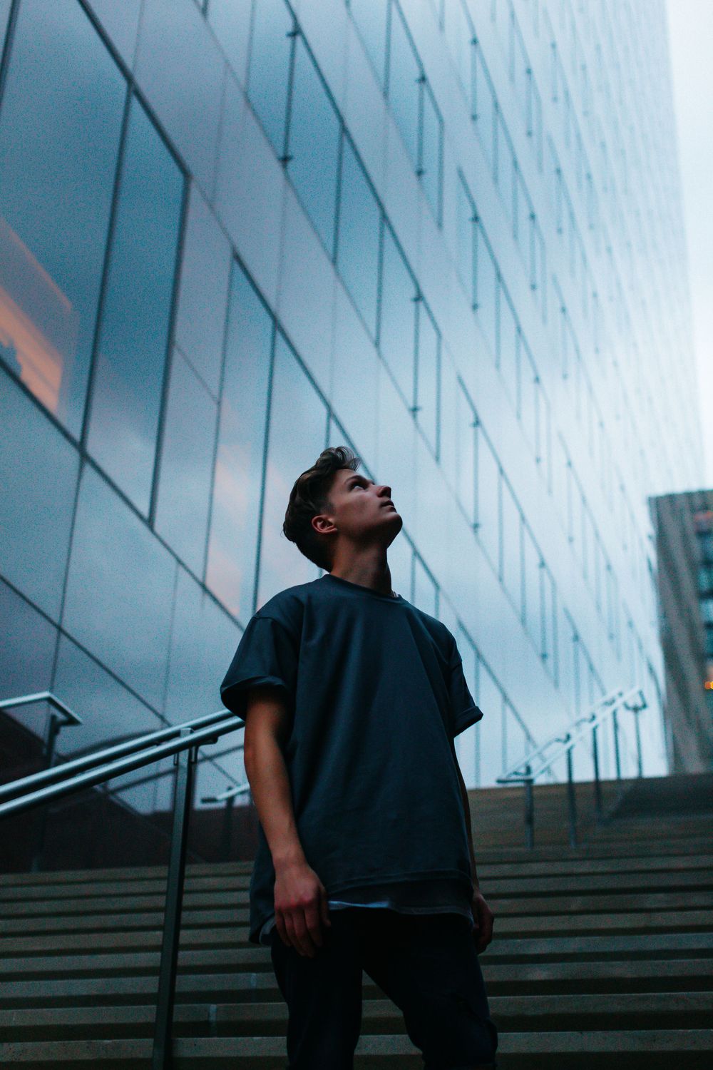 Young man in dark t-shirt standing on steps looking up at modern glass building.
