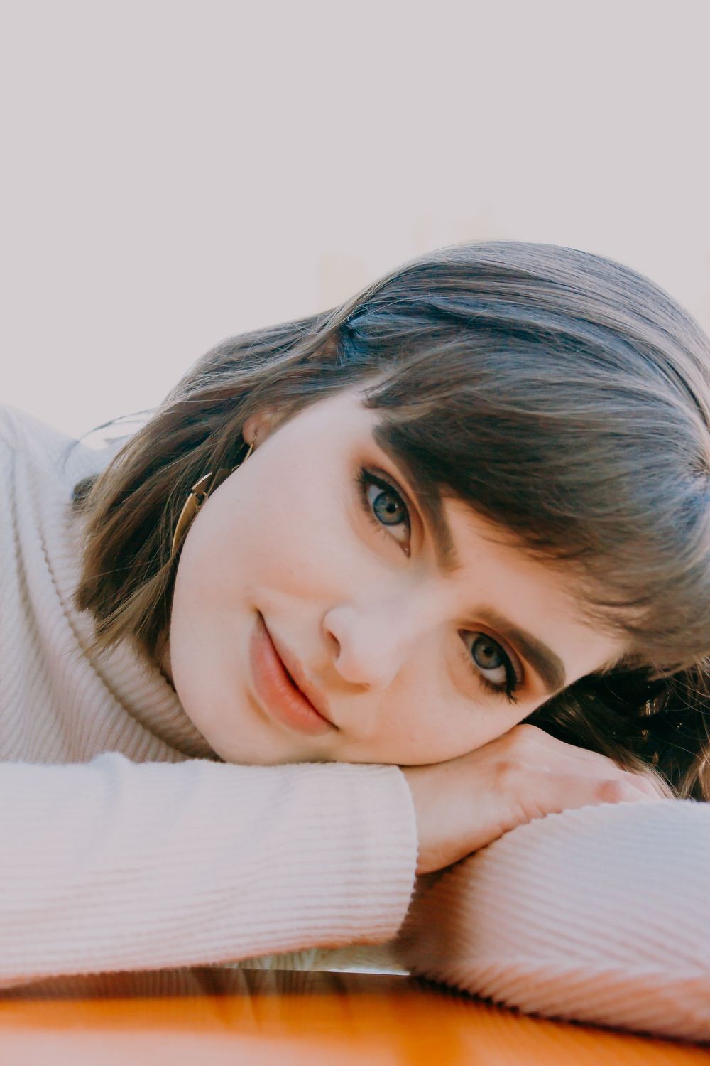 Close-up portrait of young woman with blue eyes resting chin on folded arms.