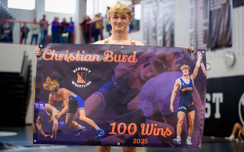 Christian Burd stands with a custom “100 Wins” banner, celebrating his wrestling milestone with family and friends.