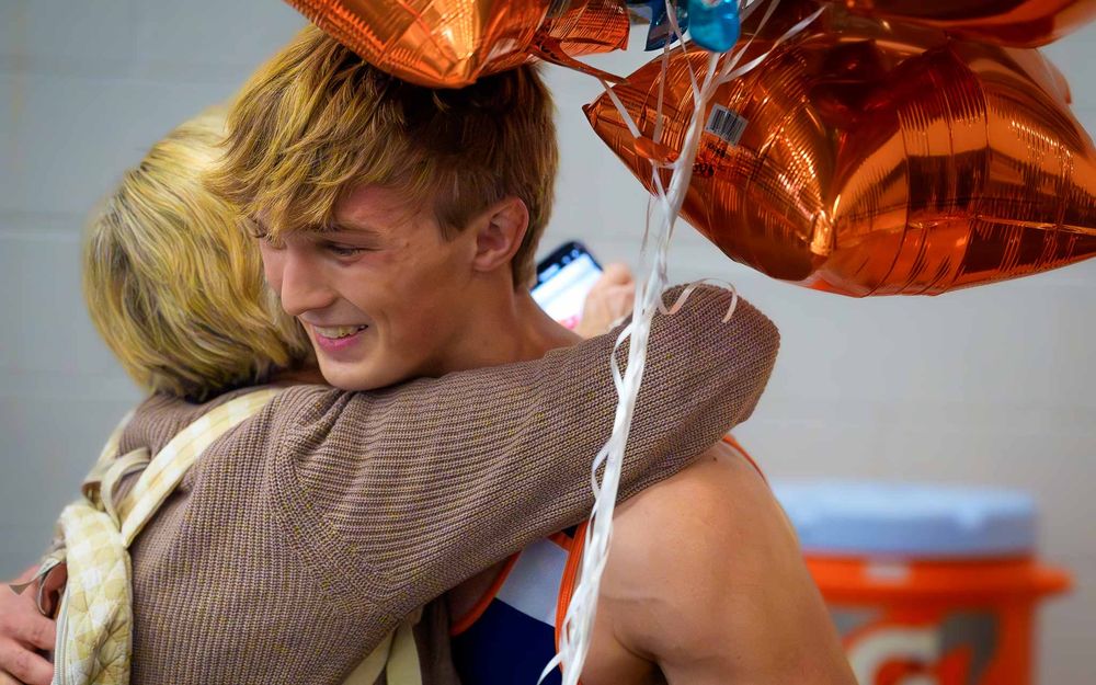 Christian Burd hugs a family member while holding celebratory balloons after reaching 100 career wrestling wins.