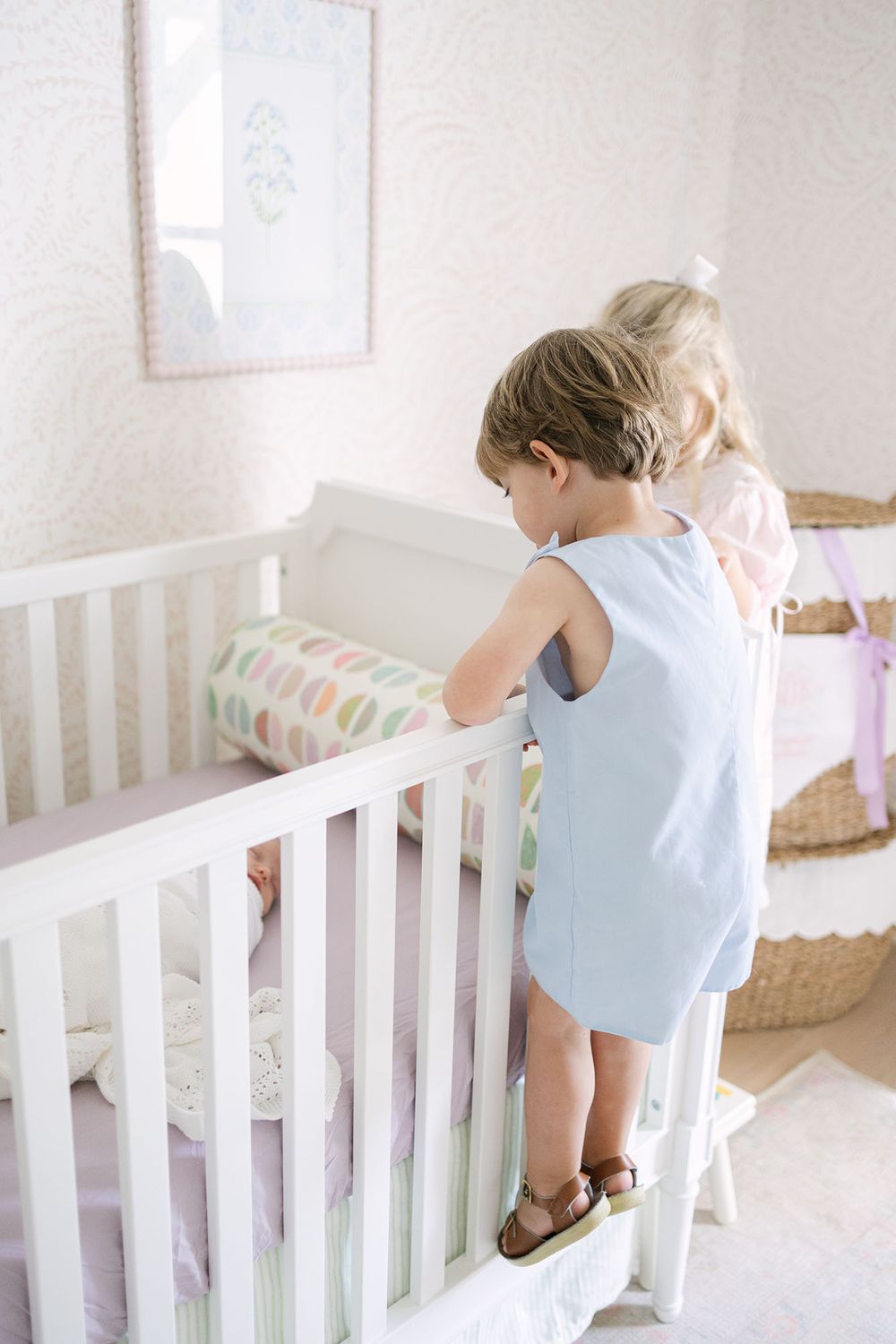 Boy and girl siblings peeking over the side of the crib at their newborn baby sister.