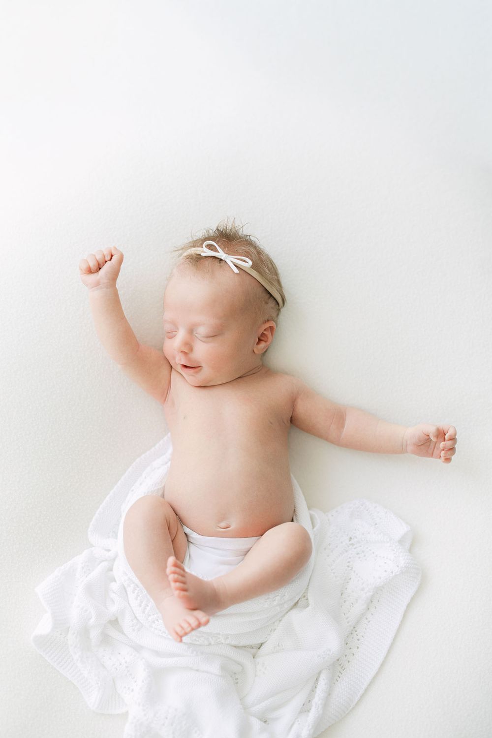 Baby girl stretching on white sheet captured by Mobile, AL newborn photographer.