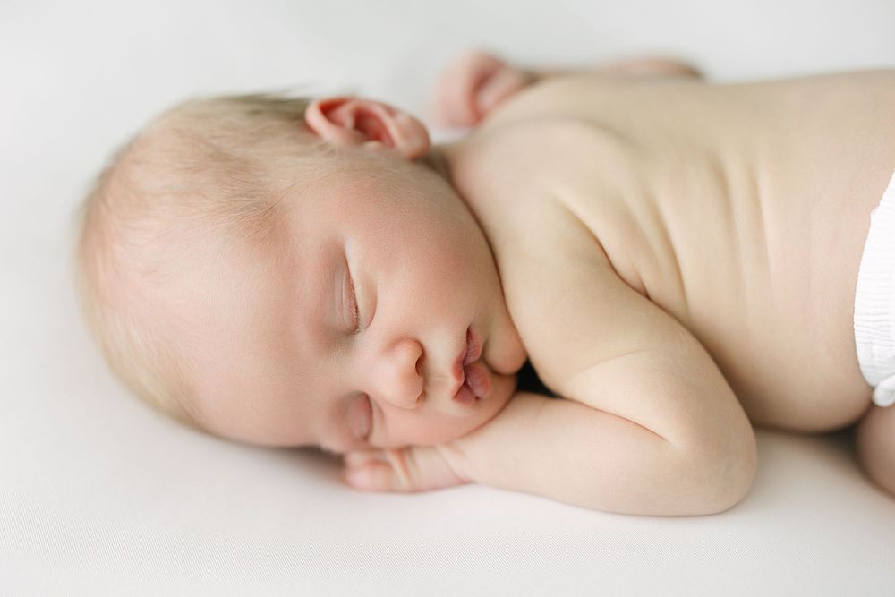 Newborn baby laying on belly on white sheets captured by Mobile, AL Newborn Photographer.