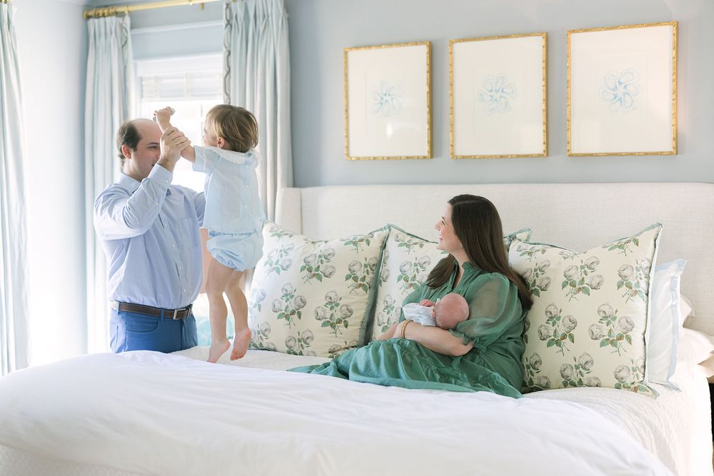 Family of 4 sitting on a bed with toddler jumping with dad, captured by Mobile, AL Newborn Photographer