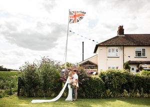 Bride and groom kissing in garden beneath Union Jack flag and colorful bunting at UK countryside wedding.
