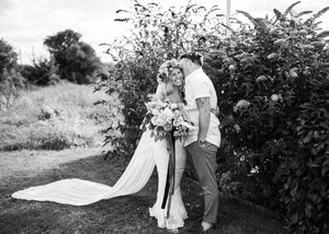 Black and white photo of bride and groom sharing a tender moment beside lush garden greenery.