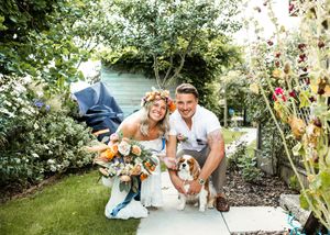 Happy couple crouching with their Cavalier King Charles Spaniel dog in a lush wedding garden.