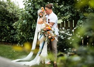 Bride and groom sharing a romantic kiss while holding a large boho bouquet in a garden setting.
