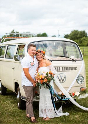 Bride and groom pose in front of vintage VW camper van at outdoor boho farm wedding.