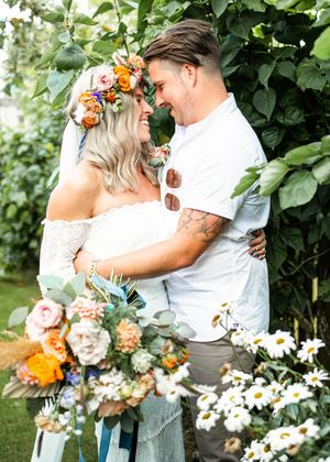Bride and groom gazing lovingly at each other surrounded by daisies and lush green garden foliage.