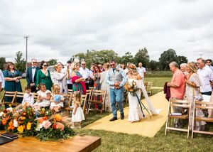 Bride walking down yellow aisle runner with escort at outdoor rustic wedding ceremony.