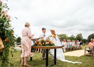 Couple exchanging vows at outdoor wedding ceremony with floral arrangements on rustic table.