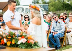 Bride and groom holding hands during outdoor wedding ceremony with smiling guests seated nearby.