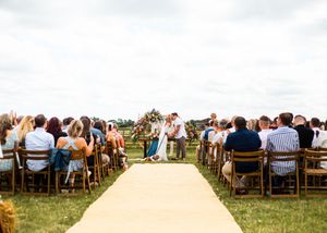 Wide shot of outdoor wedding ceremony with guests seated along yellow aisle runner.