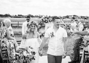 Newlyweds walk hand in hand down the aisle as guests celebrate at an outdoor farm wedding ceremony.