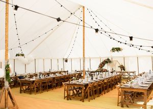 Elegant white wedding marquee with string lights and long wooden farm tables set for wedding reception.